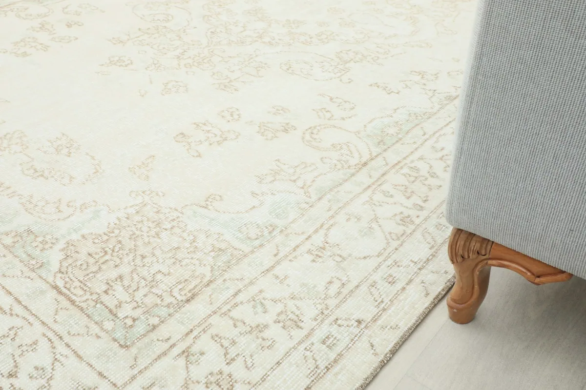 Partial view of the rug on the floor next to a light-colored armchair, demonstrating its scale in a room.
