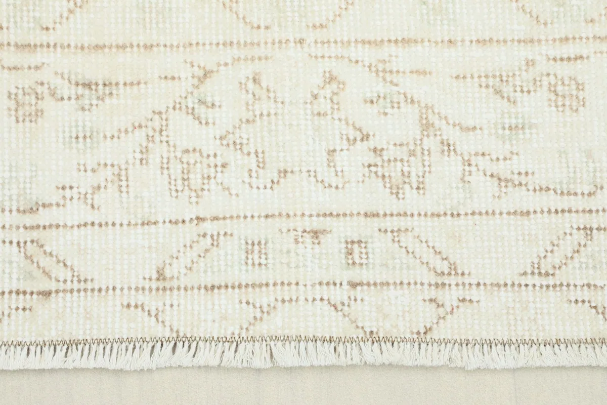 Close-up view of the rug's border and fringe, showing the intricate beige patterns and texture.