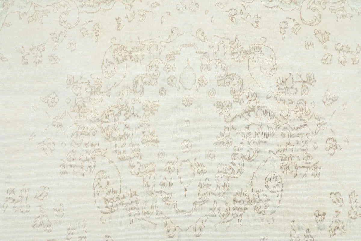 Detailed view of the central medallion design on the ivory rug, highlighting the faded beige motifs.