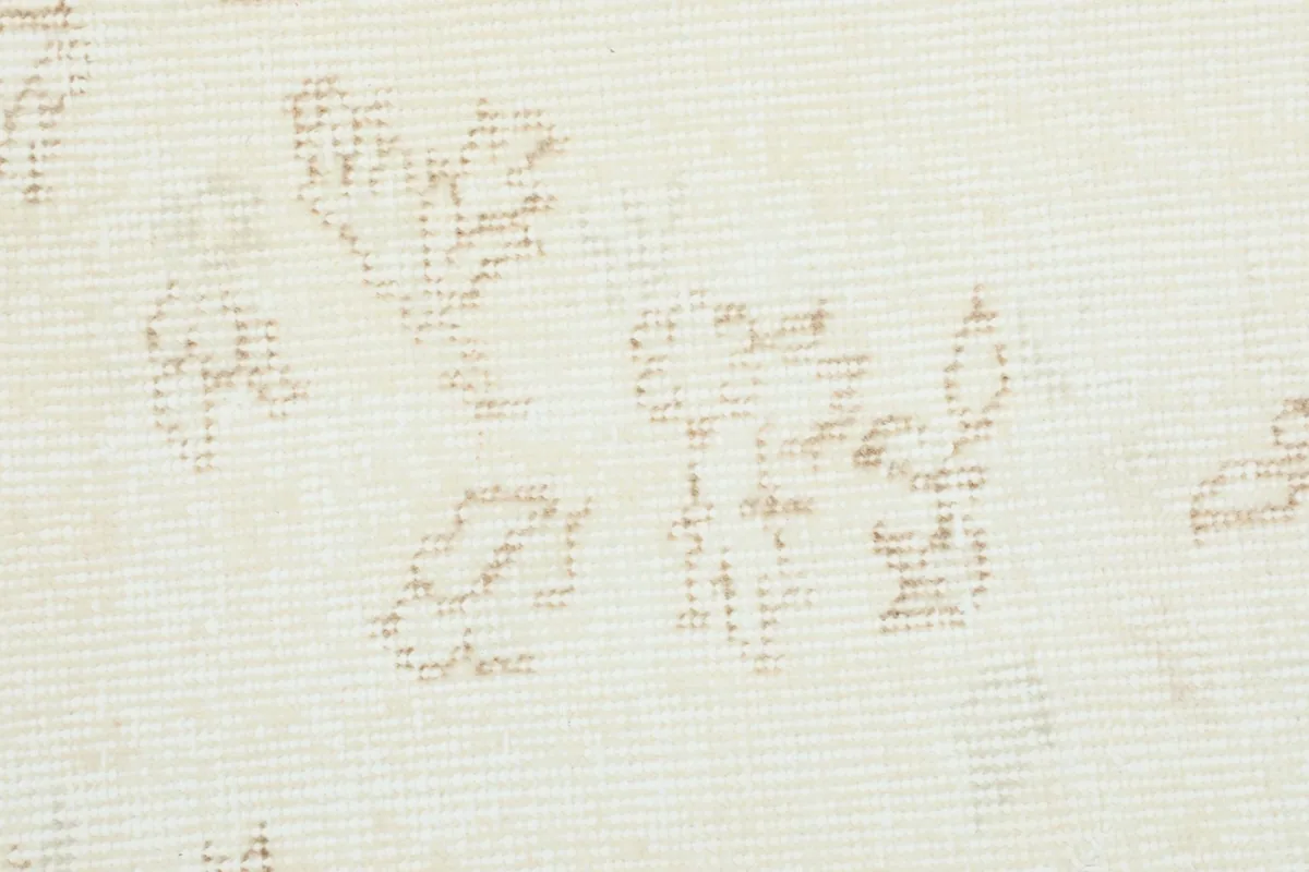 Close-up of the rug's surface, revealing the low pile and textured, distressed beige floral patterns.