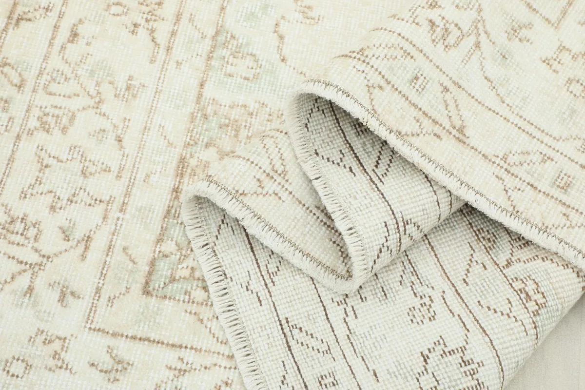 Close-up showing the low pile and weave structure, with a partial fold revealing the rug's thickness.
