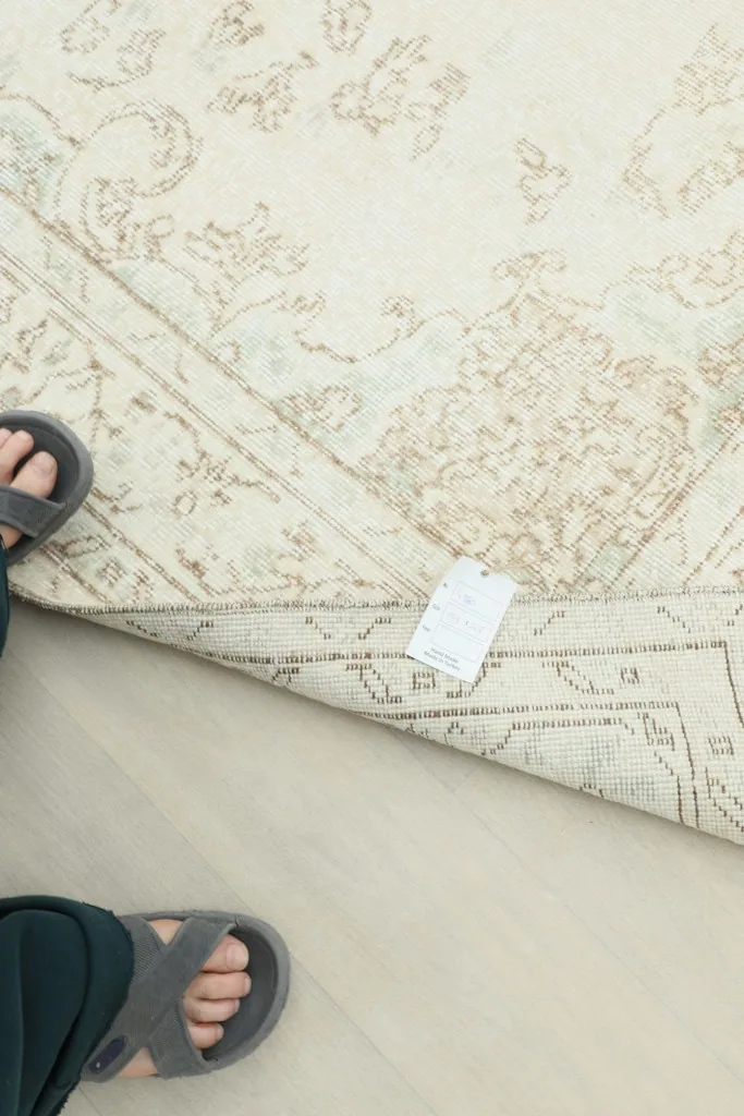 Overhead view of the rug's back, showing the hand-knotted construction and a tag, with feet in sandals.