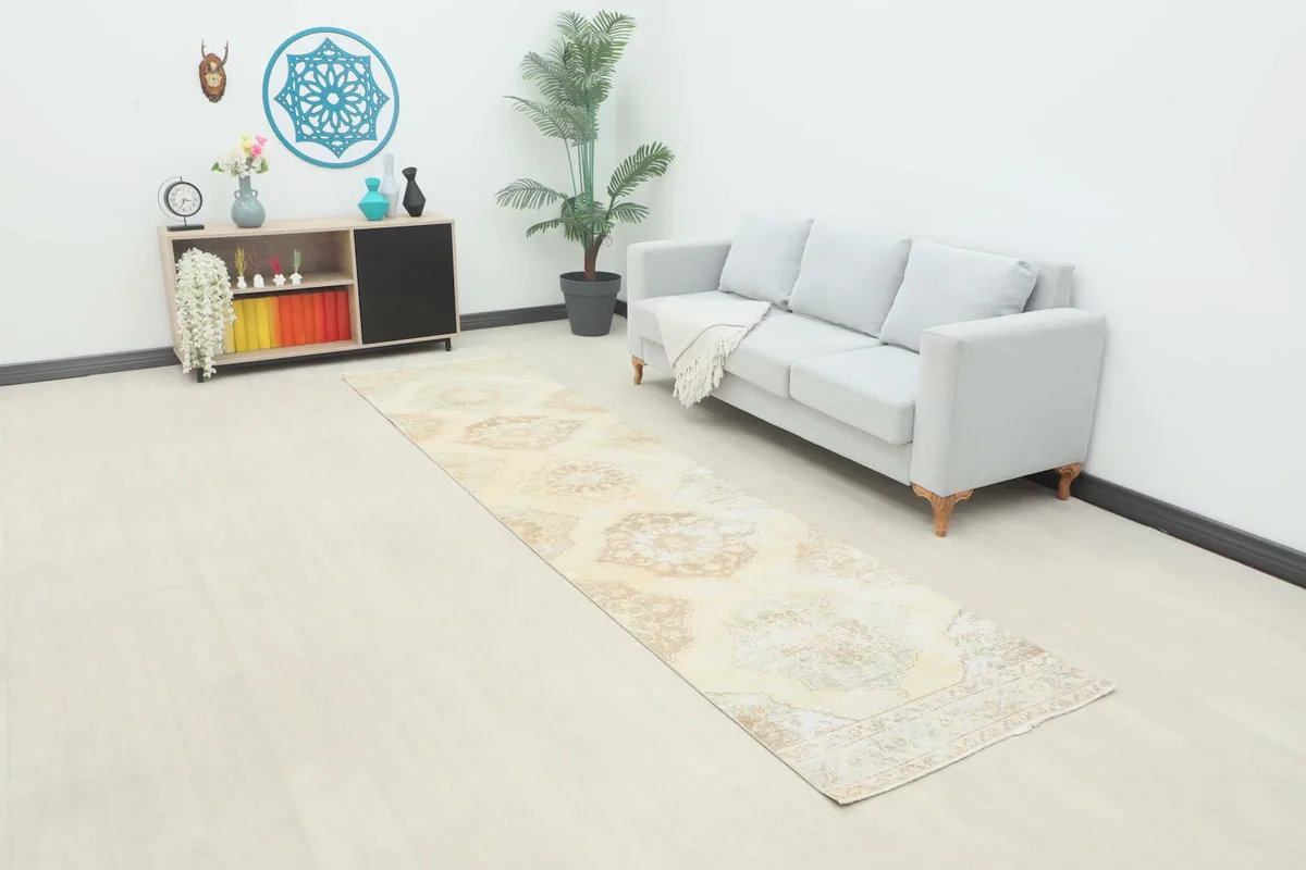 Ivory vintage runner rug displayed in a room setting next to a sofa and cabinet.