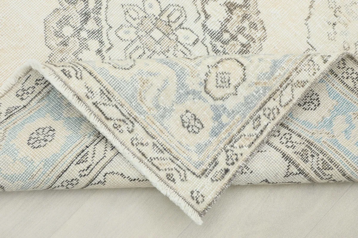 Folded corner of the rug, revealing the soft blue and ivory tones in the pattern.