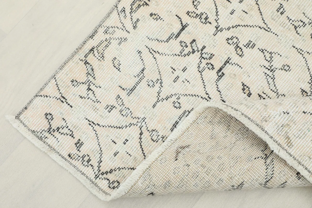Corner of the ivory and charcoal rug folded to show the back and foundation.