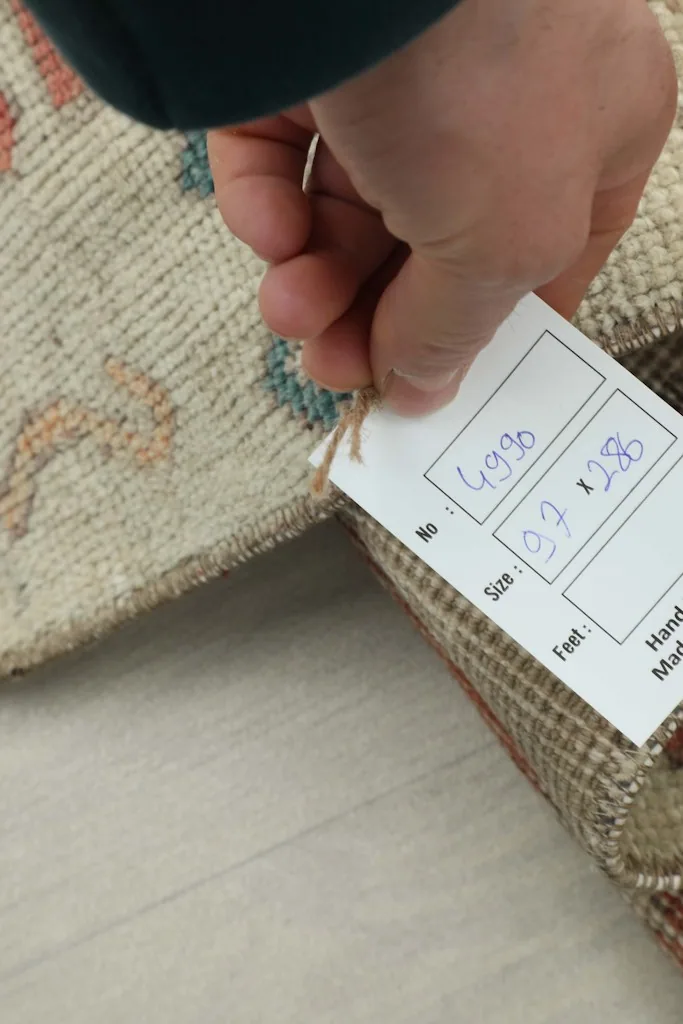 Hand holding a tag with the rug's dimensions (97 x 286 cm) and unique identification number.
