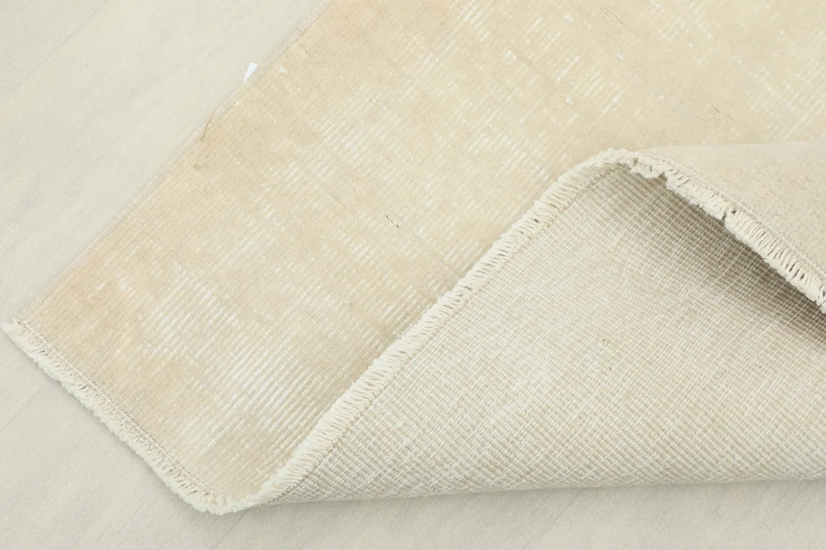 Corner of the rug folded back, showing the cotton foundation and the reverse side of the hand-knotted wool.