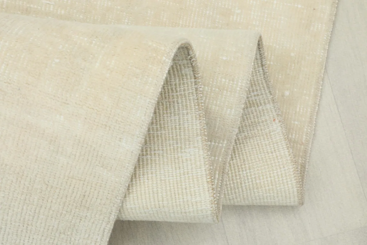 Side view of the rug folded, showing the thickness of the low pile and the construction.