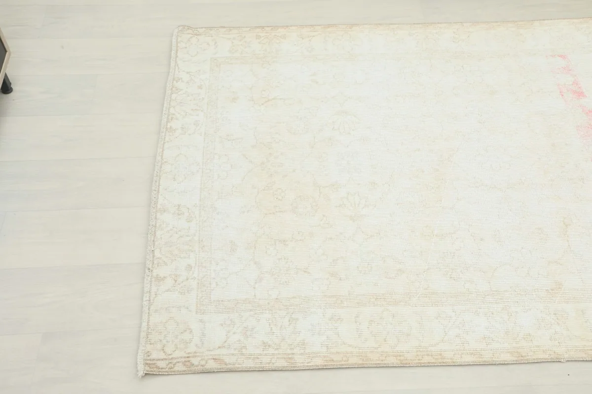 Corner detail of the cream and rose vintage rug, highlighting the subtle border pattern and distressed areas.