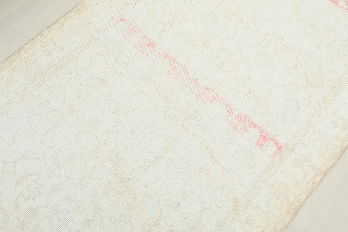 Detailed view of the faded rose color and worn pile in the center of the cream vintage rug.