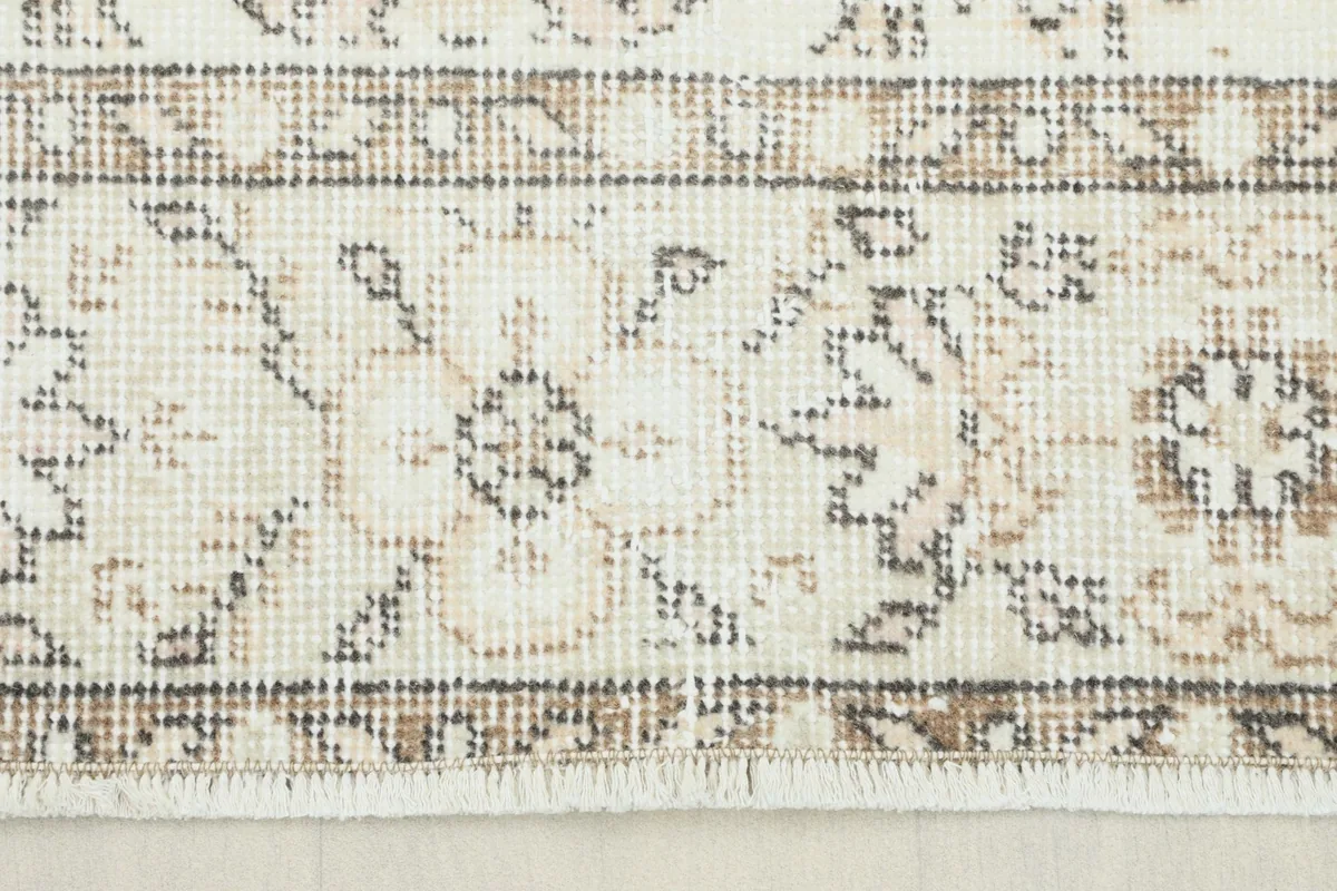 Close-up view of the rug's border showing tan and gray floral patterns and fringe