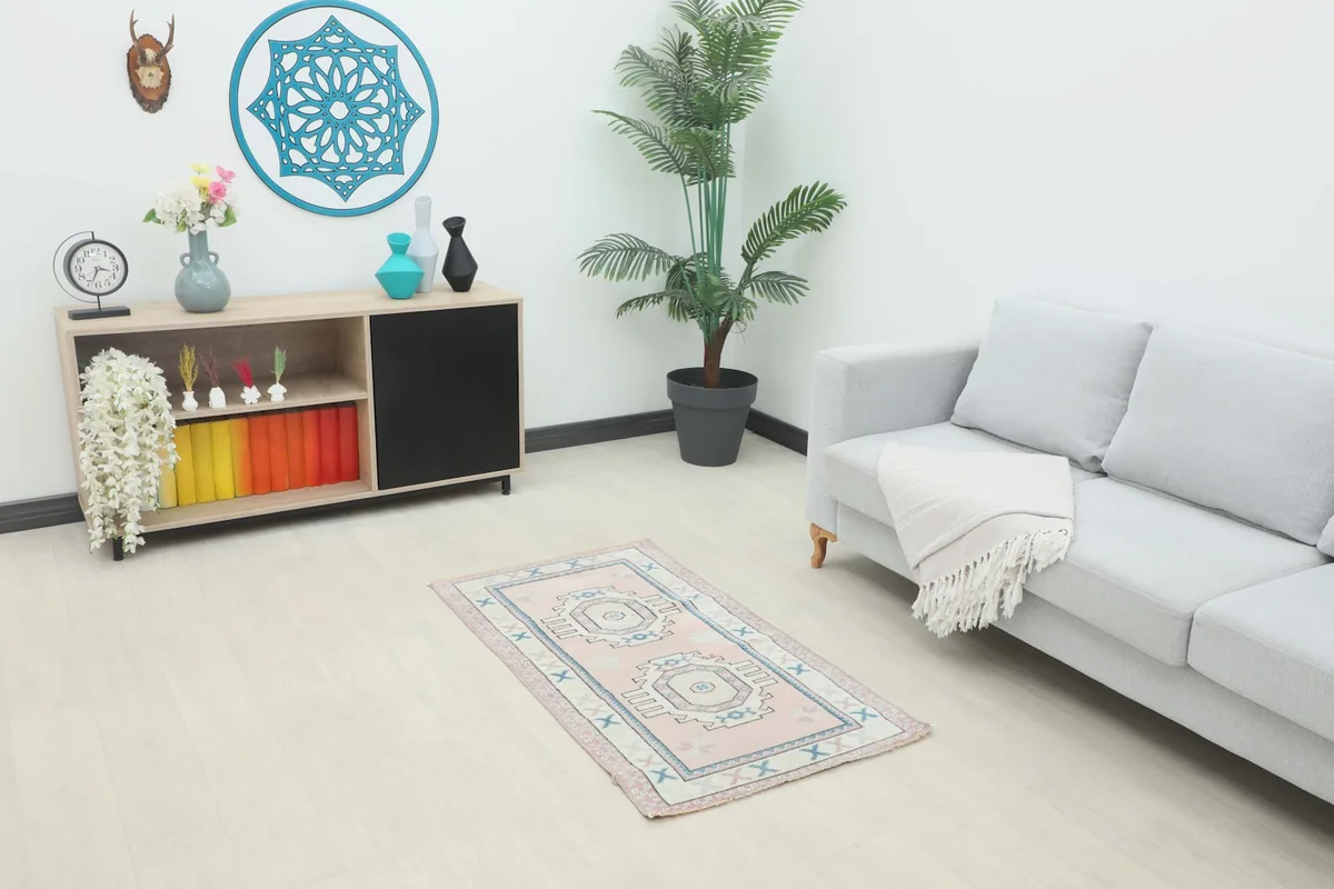 Pink vintage rug placed in a living room setting with a light gray sofa and wooden cabinet