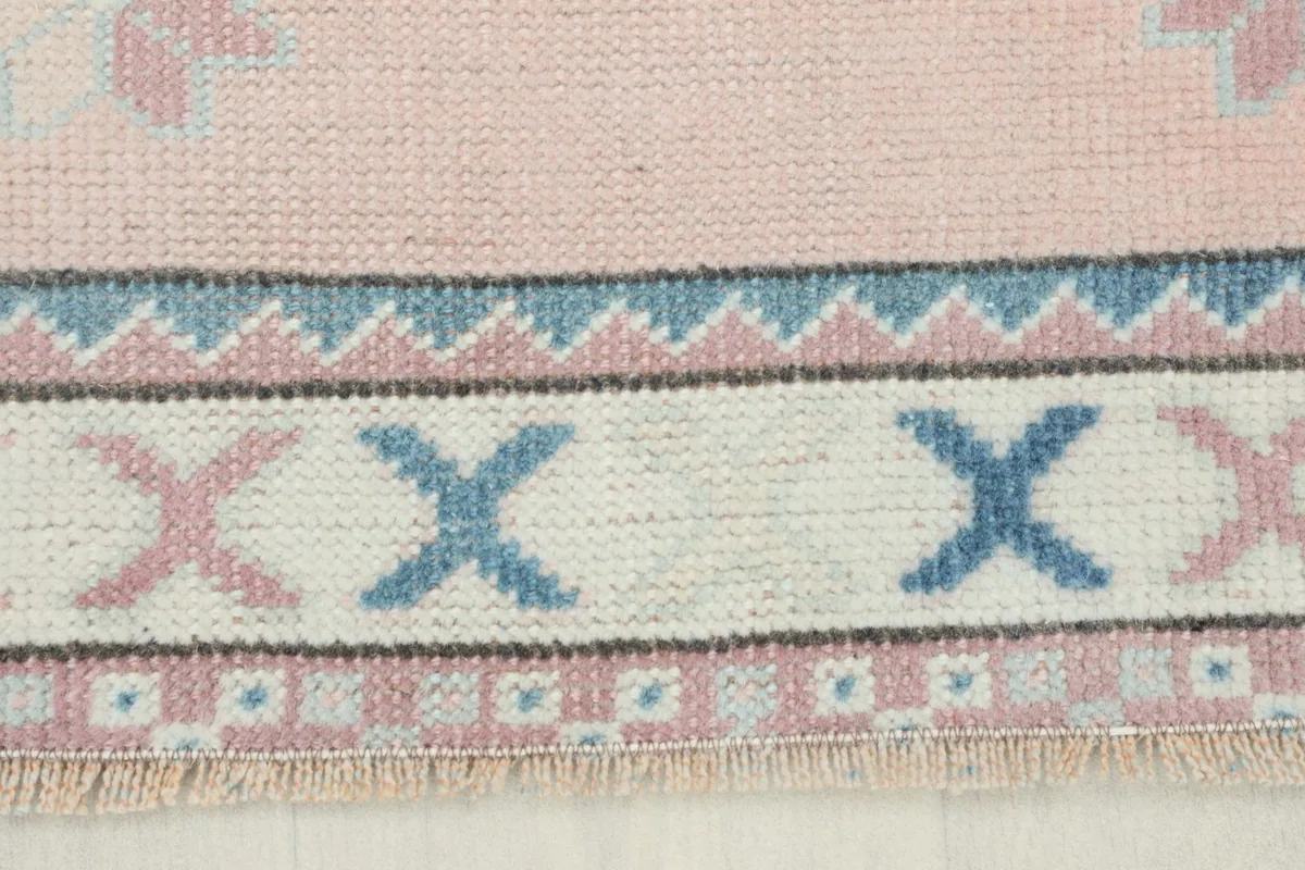 Close-up of the rug's border, featuring 'X' motifs in pink and blue, and a thin blue geometric band