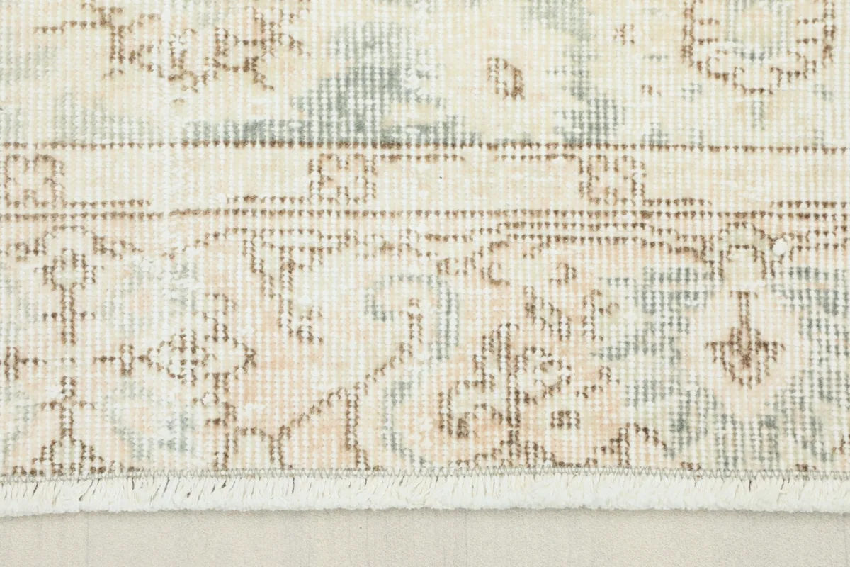 Close-up detail of the rug's border showing the subtle ivory, blue, and tan floral patterns and fringe.