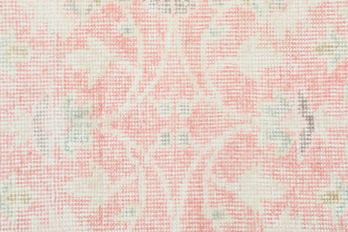 Detailed close-up of the hand-knotted wool pile and faded floral design in pink and ivory