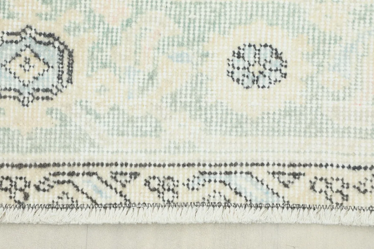 Close-up of the rug's border and field, showing subtle blue, beige, and gray tones in the hand-knotted wool pile.