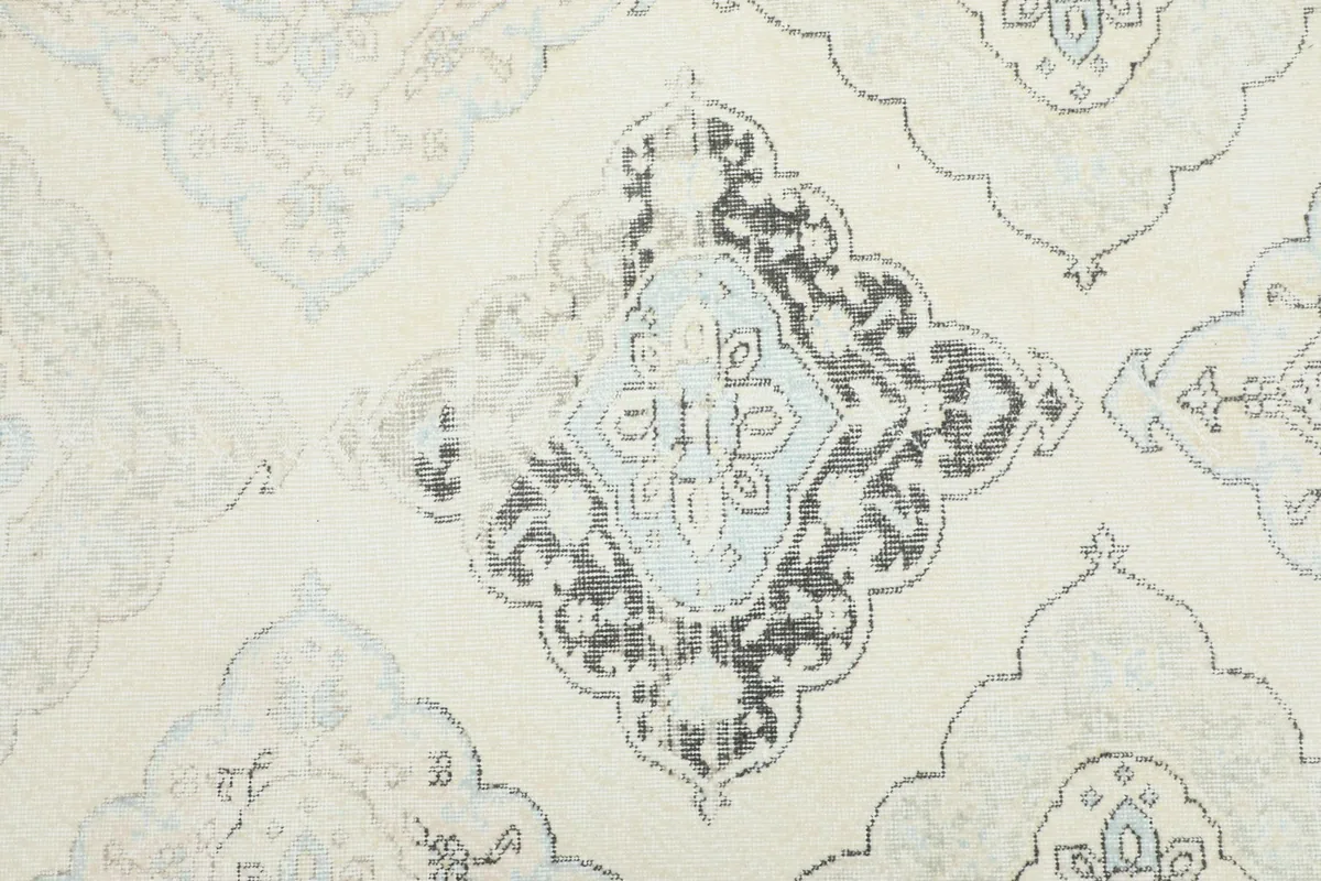 Detailed view of a central geometric medallion with distressed gray and light blue elements on a cream field.