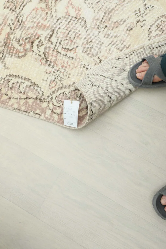 Person's feet near a rolled-back corner of the rug, showing the flexibility and thickness of the material