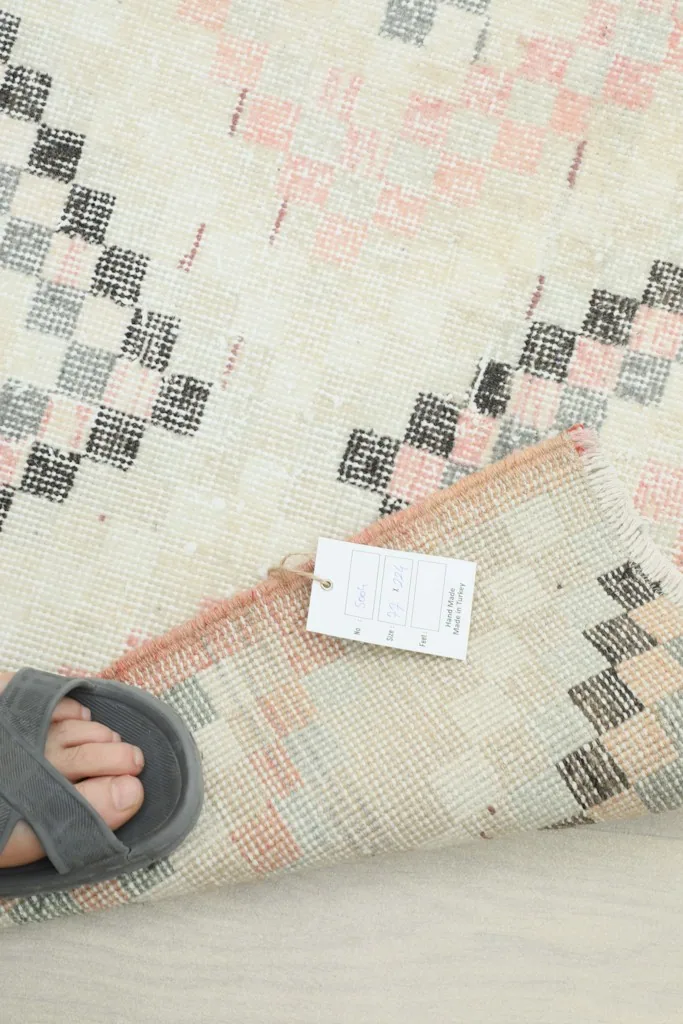 Rug corner with a sandal and product tag, providing a sense of scale and showing the rug's thickness.
