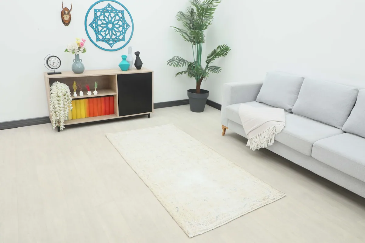 Faded beige vintage rug placed in a modern living room setting with a gray sofa and light wood furniture.