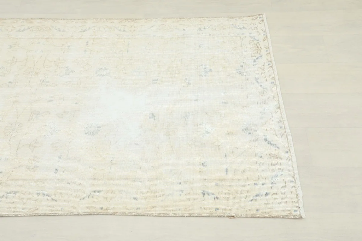 Close-up of the corner of the beige rug, showing the faded floral and geometric patterns and border.