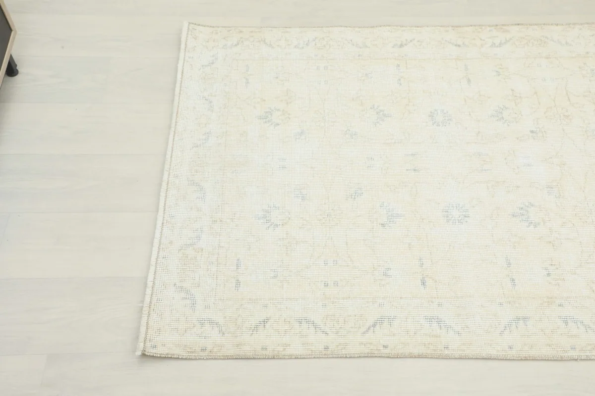 Detailed view of the rug's surface, revealing the faint blue and tan motifs against the light beige field.