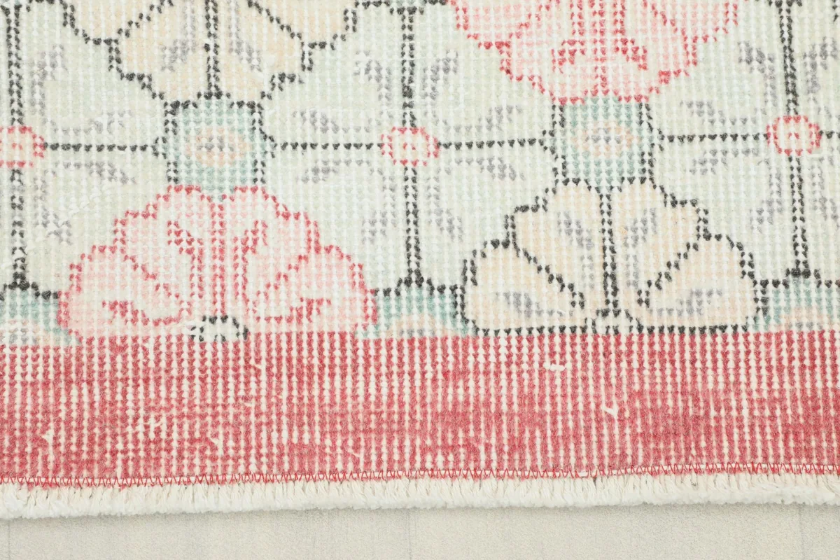 Close-up view of the rug's red border and the transition to the ivory field with pink motifs.