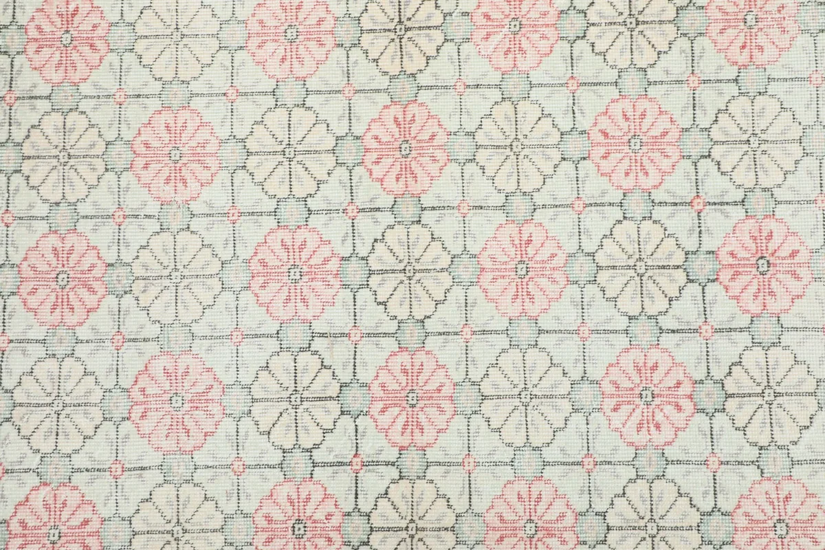 Detailed view of the repeating pink floral and gray geometric patterns on the rug's ivory field.