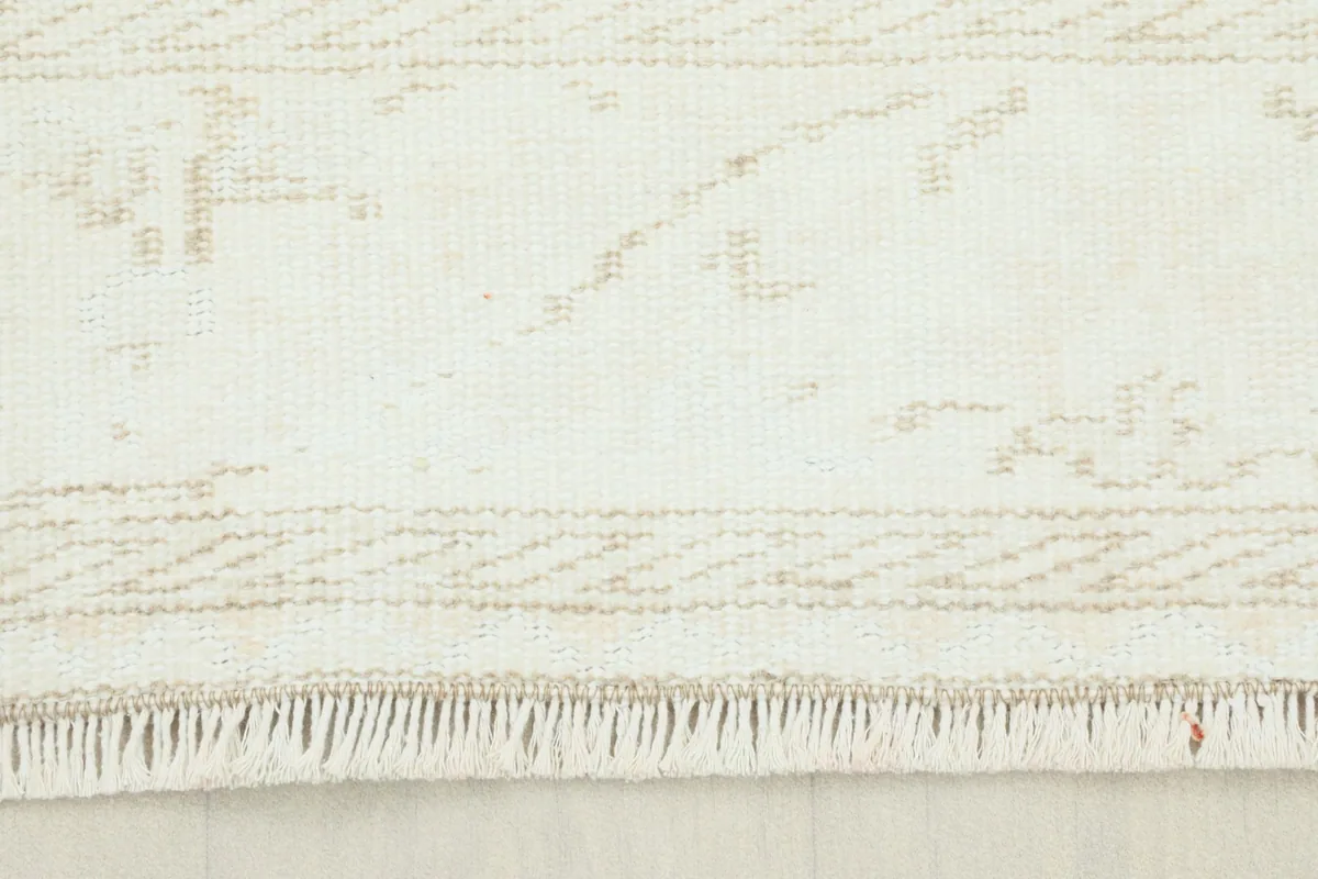 Close-up of the rug's fringe and the subtle geometric patterns at the edge.