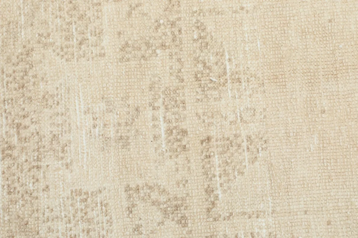 Close-up of the distressed wool pile, revealing faint tan geometric motifs on an ivory field