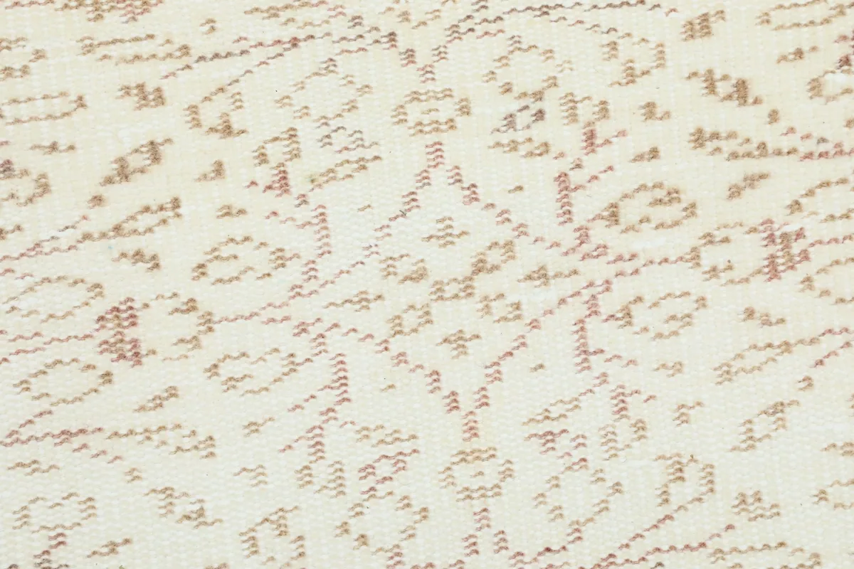 Close-up of the subtle tan and beige geometric motifs within the rug's cream field