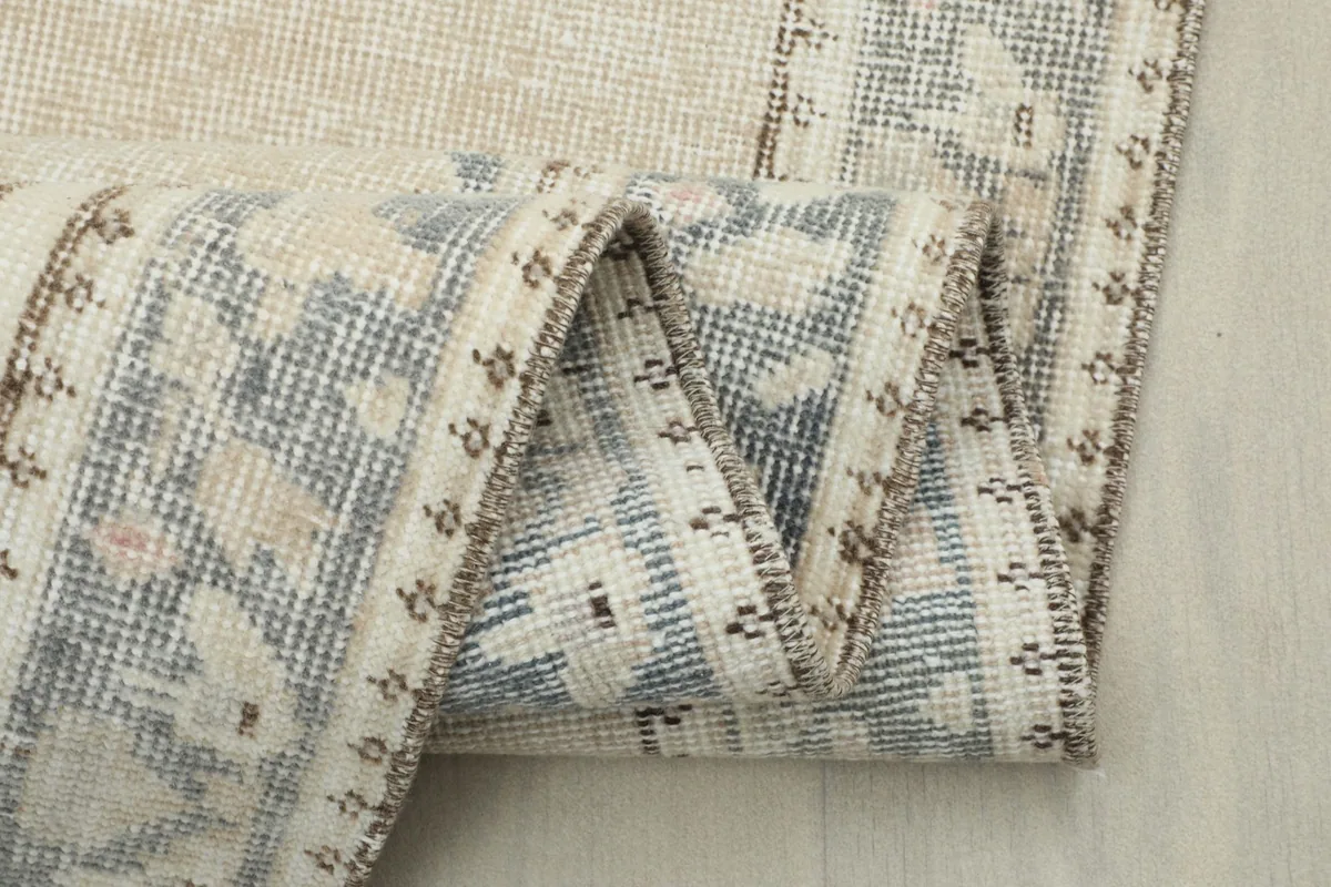 Close-up of the folded rug, emphasizing the weave and the subtle blue and tan tones in the border