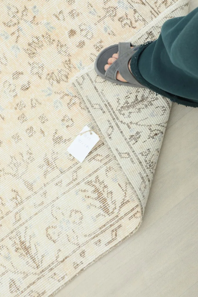 Underside of the rug visible as a foot steps on a folded corner, showing the tag