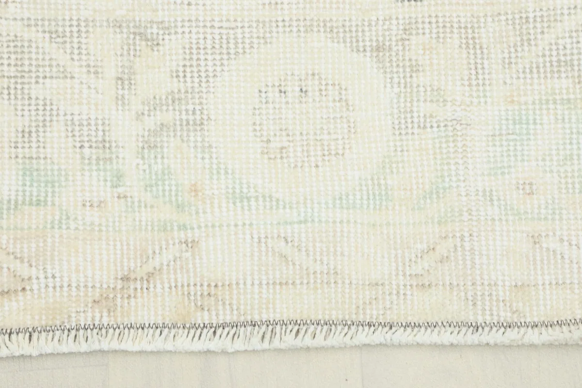 Close-up of the rug's edge showing the faded ivory and gray pattern and fringe