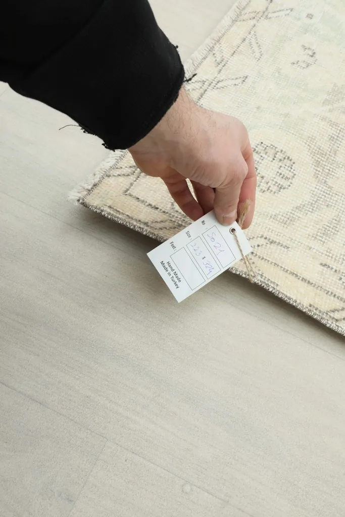 Hand holding a product tag, showing the reverse side of the rug and its label