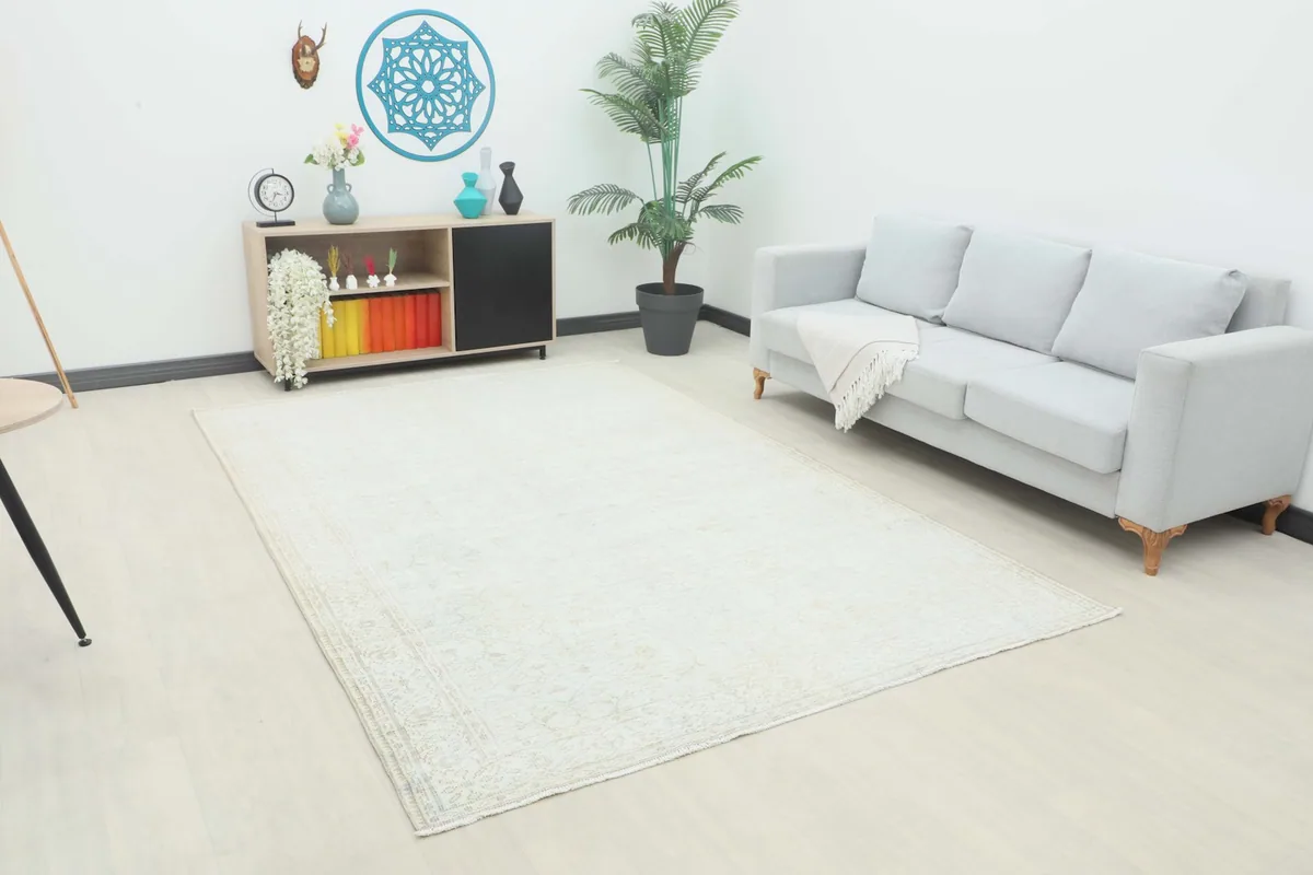 Cream vintage rug displayed in a living room setting with a light gray sofa and wooden console.