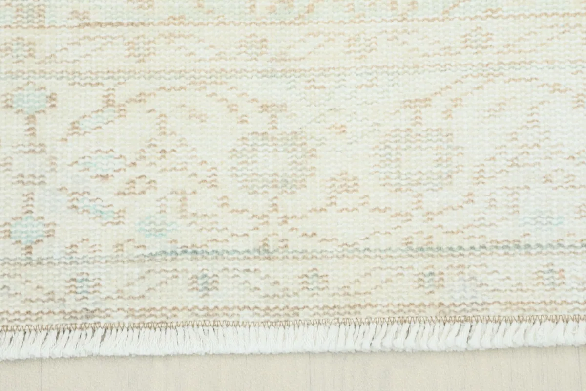 Close-up detail of the rug's border showing subtle beige and blue floral motifs and fringe.