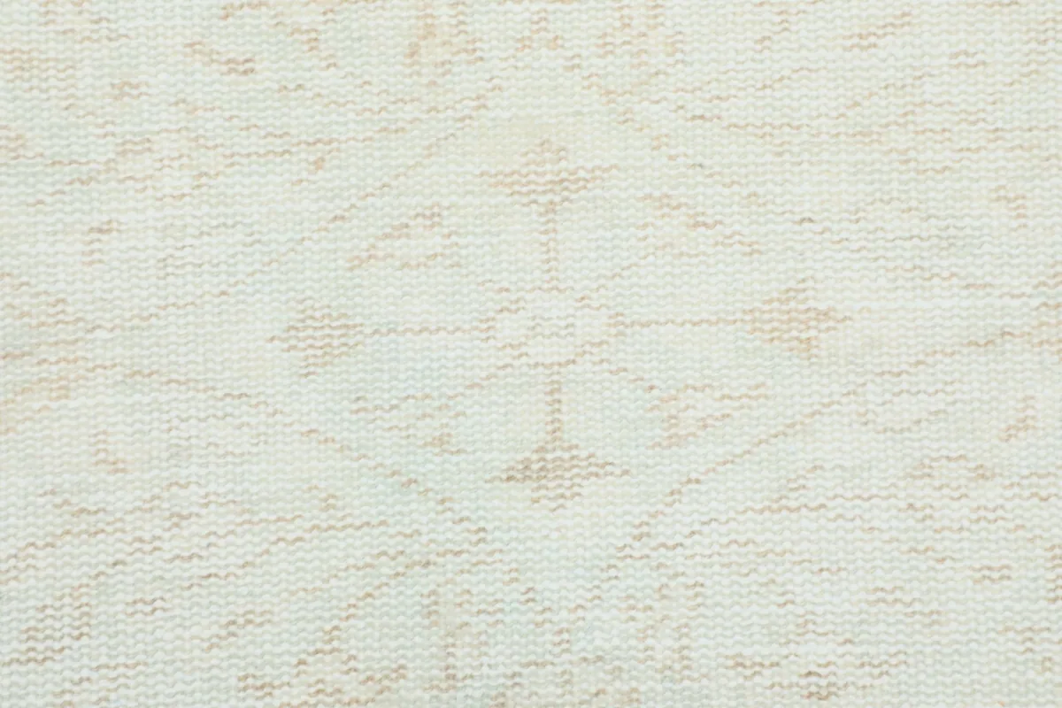 Tight close-up of the rug's low pile and delicate cream and beige hand-knotted patterns.