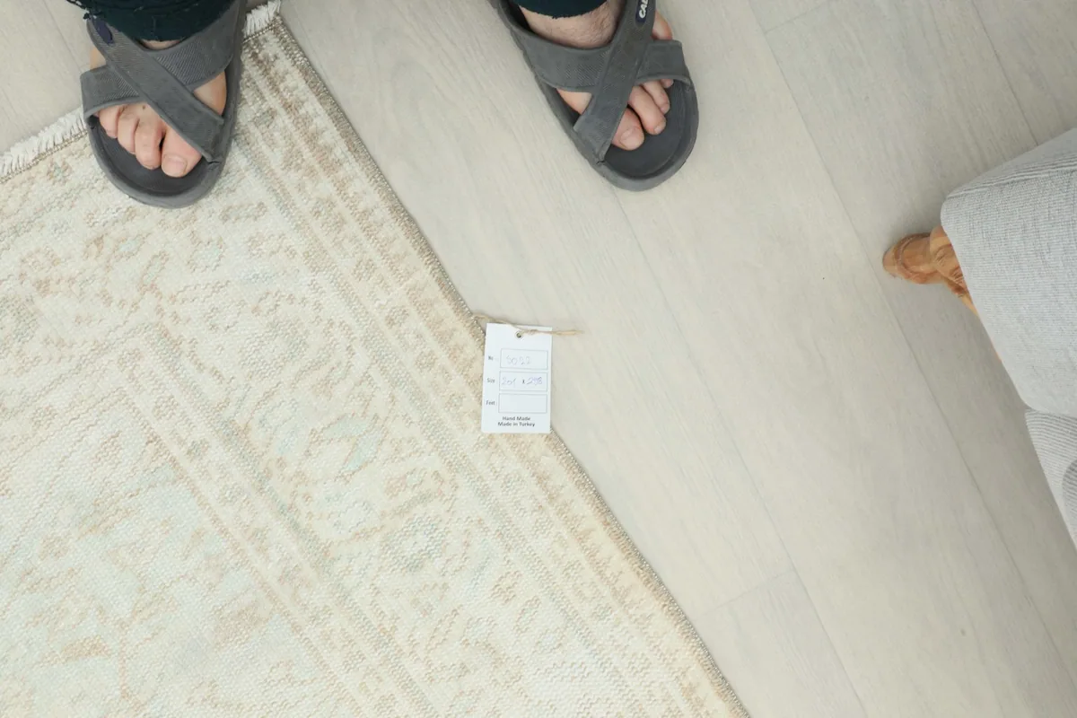 Overhead view of a person's feet on the floor next to the rug, with a size tag for scale.