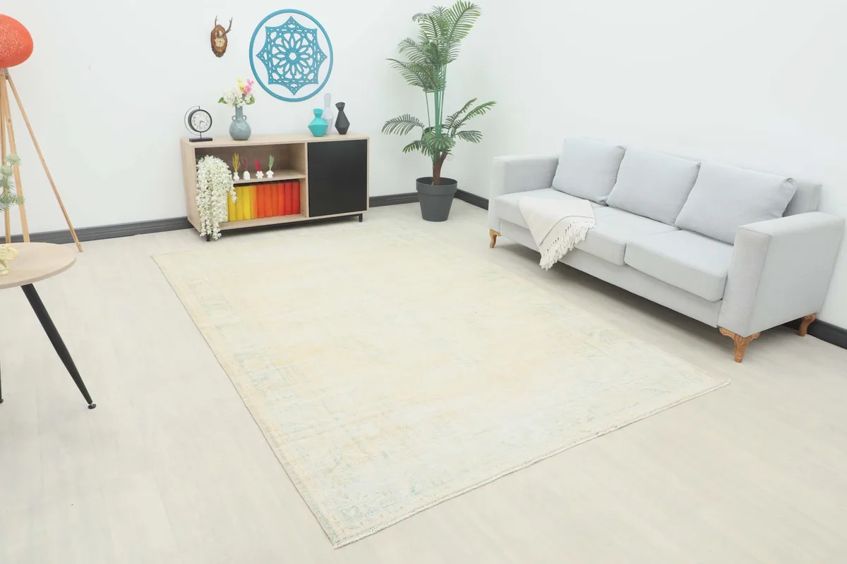 Ivory and blue vintage Anatolian rug placed in a living room setting with a light gray sofa and wooden cabinet.