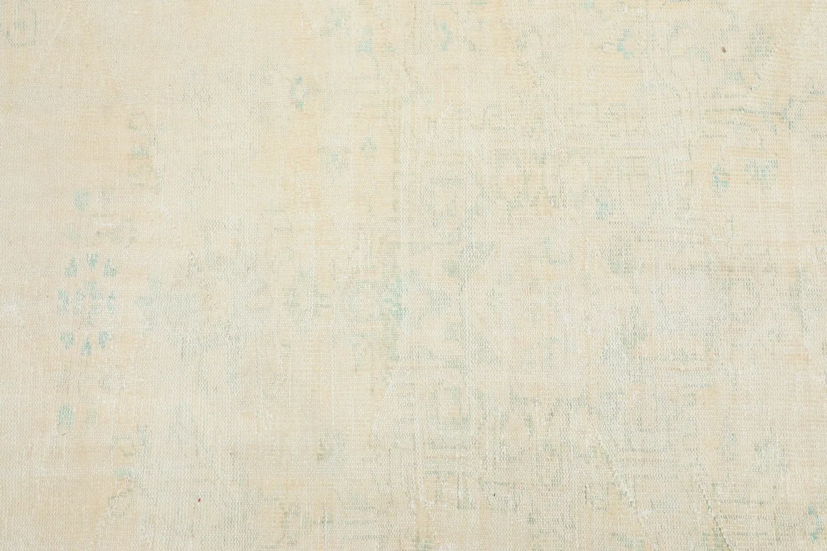Detailed view of the subtle ivory field with muted blue geometric patterns and soft patina.
