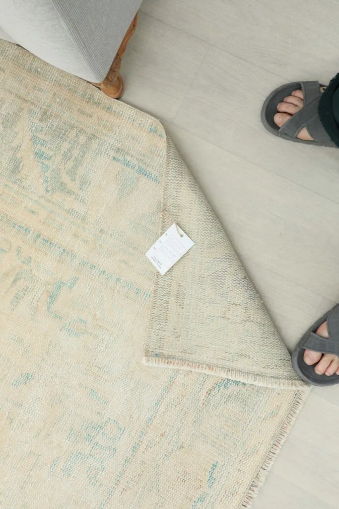 Overhead view of a corner of the rug with a tag, next to a person's feet in sandals.