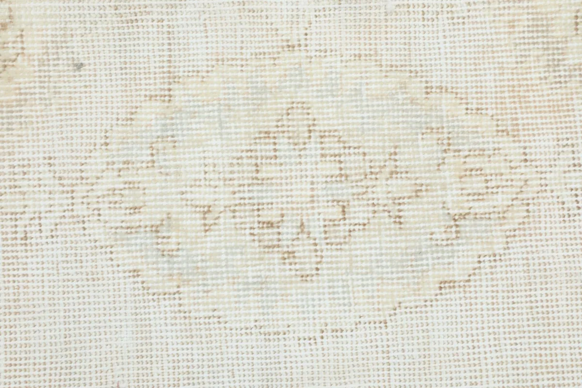 Close-up showing a central motif with faded beige and ivory colors and low pile.