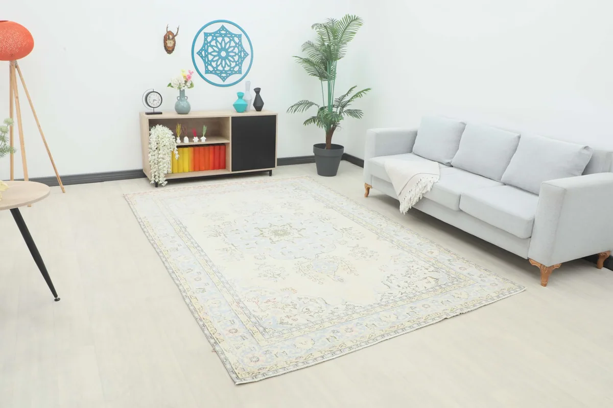 Angled view of the cream and blue vintage rug in a living room scene with a gray sofa and wooden cabinet.