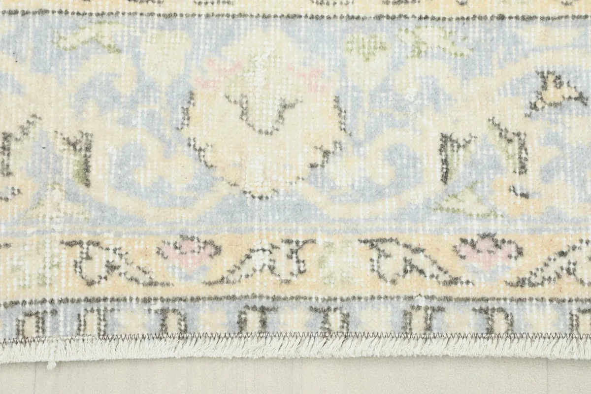 Close-up of the rug's border showing soft blue, beige, and pink floral patterns and fringe.