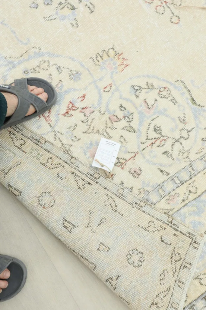 View of a person's feet and a tag near a folded corner of the rug, illustrating scale and back.