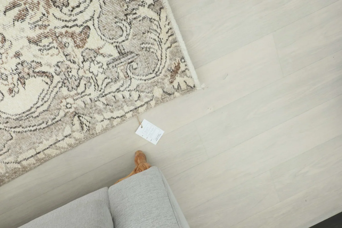 Overhead shot of the rug's corner with a tag, next to a light wood floor and sofa leg