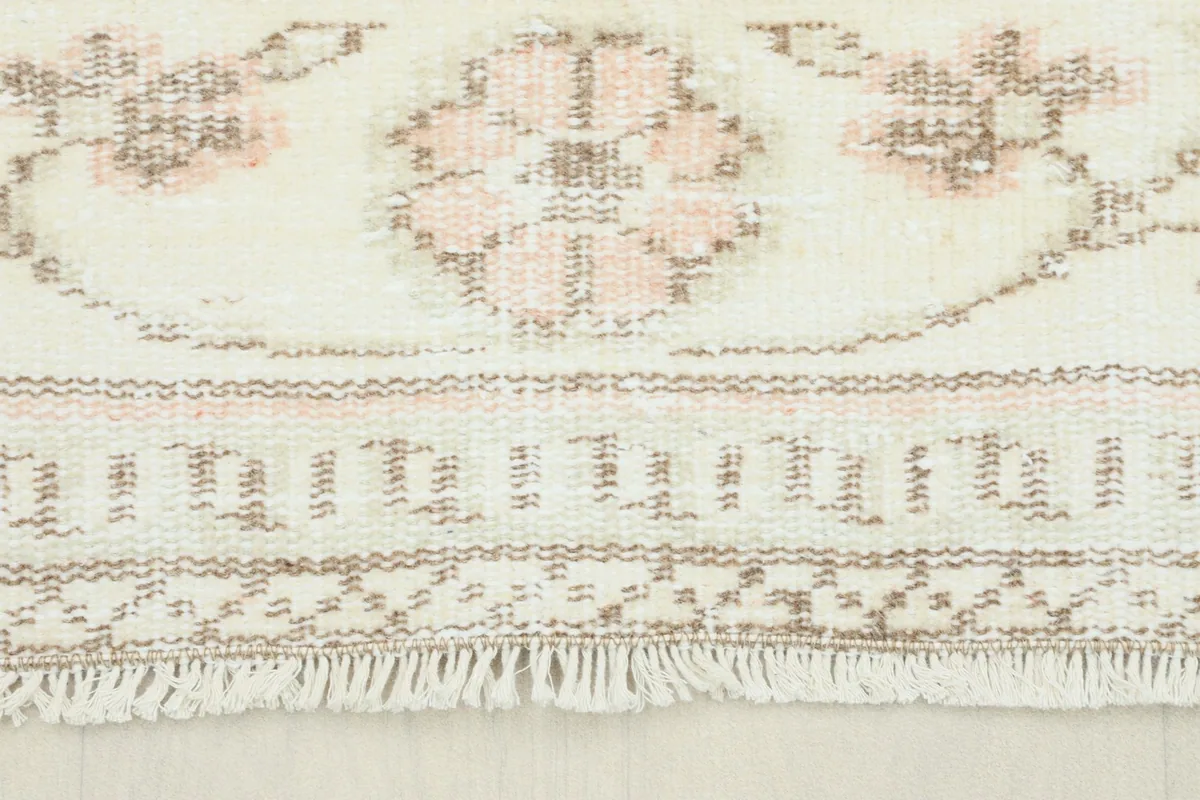 Close-up view of the fringe and border details of the vintage rug, showing rose and ivory tones