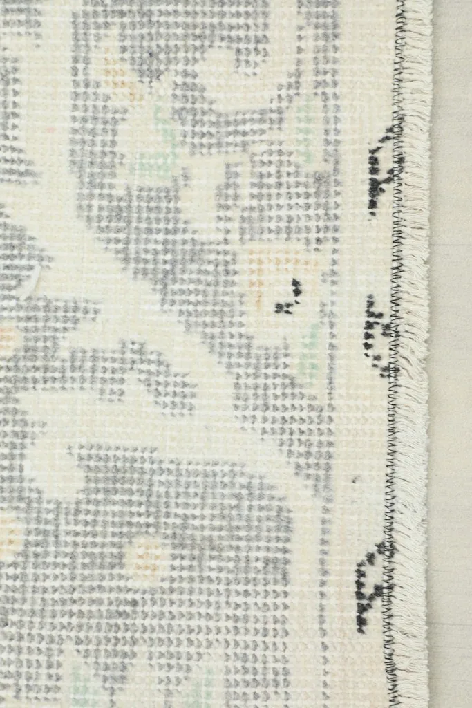 Close-up of the rug's edge showing the intricate gray and ivory border pattern with subtle green details.