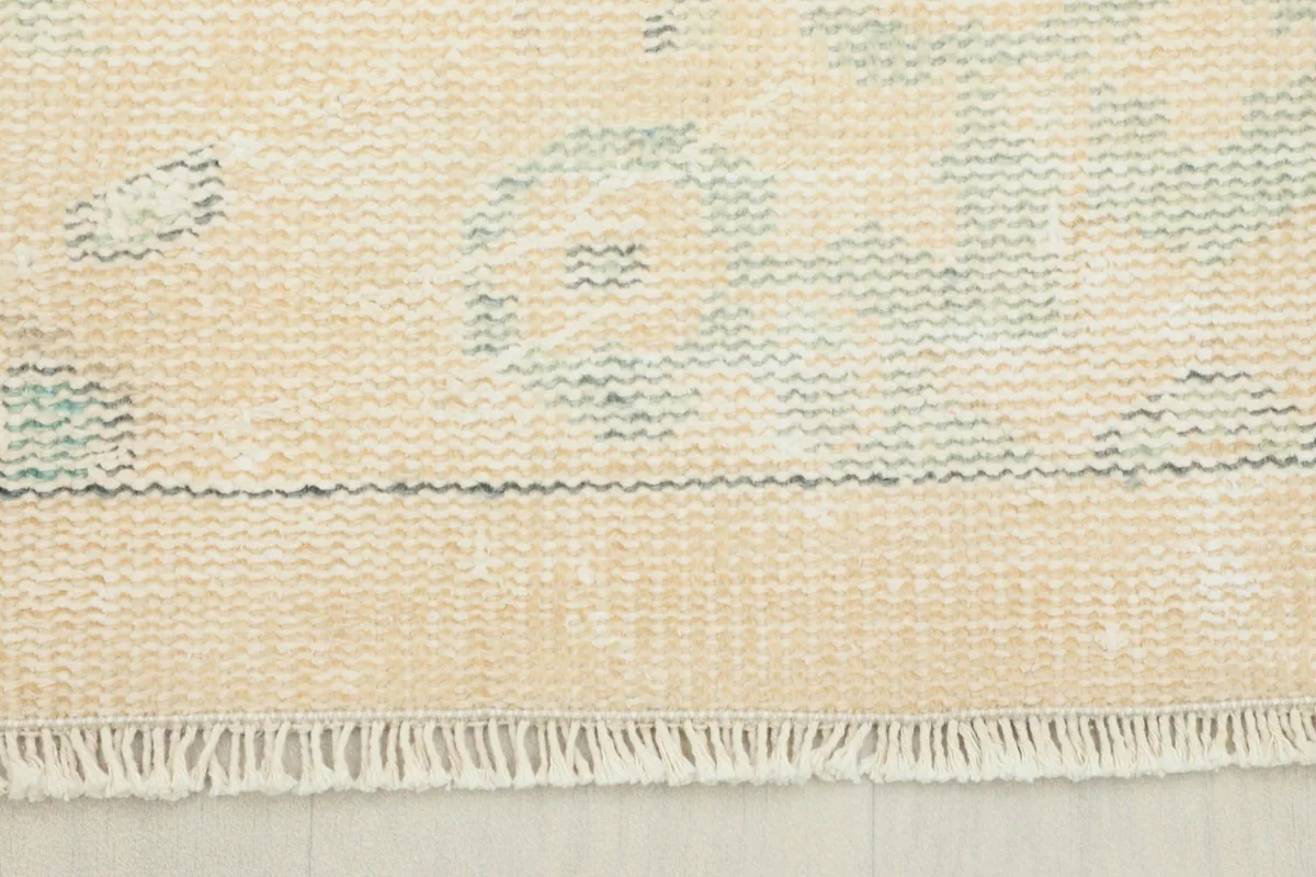 Close-up view of the low wool pile and fringe of the vintage rug, showing texture and muted colors.